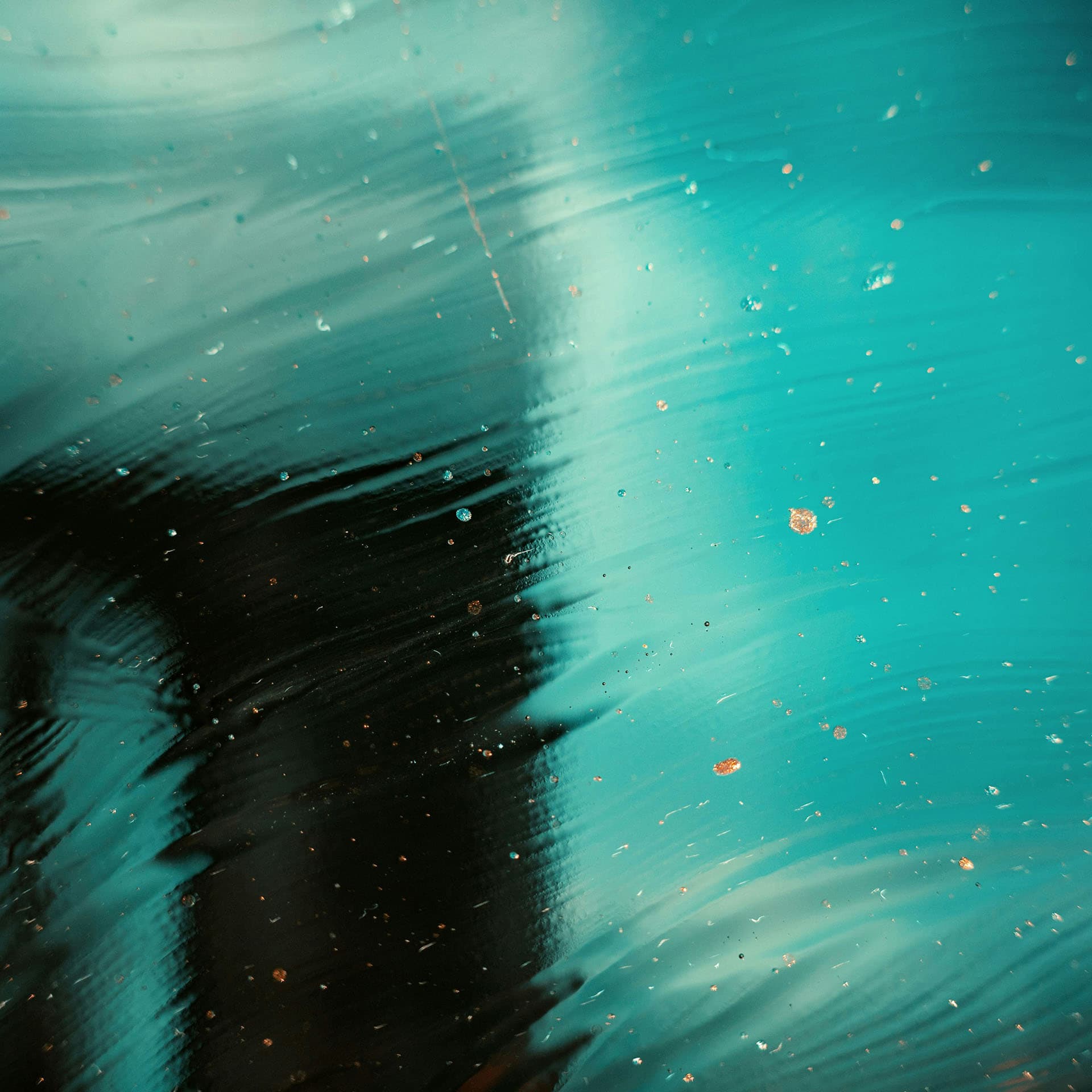 A black and teal textured surface that resembles water with golden glitter scattered on top.