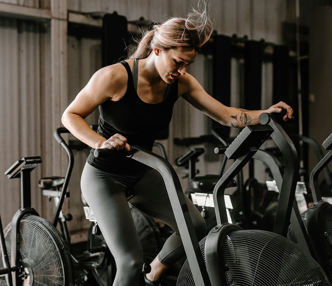 A woman in sports attire intensely exercising on a cycling machine at a gym.