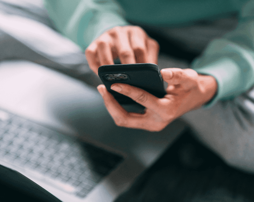 Close-up of a person sitting and using a smartphone, with a blurred keyboard visible in the background.