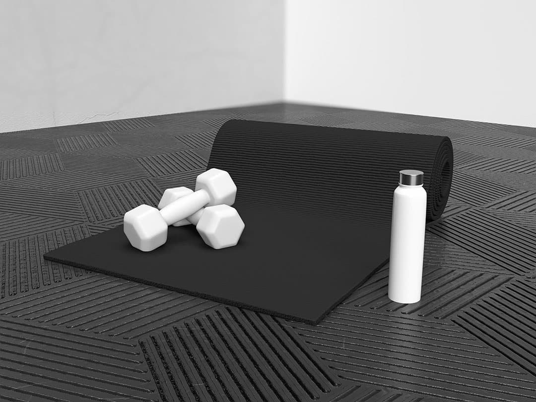A dark grey yoga mat half rolled out on a geometric patterned grey floor, with two white dumbbells resting on top and a white water bottle placed nearby.